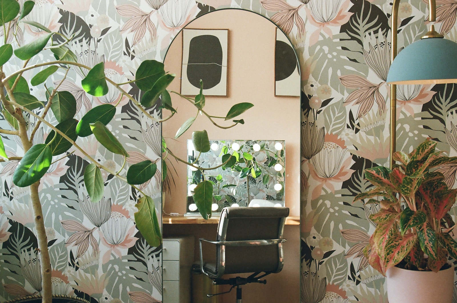 a room with a desk, chair, mirror and plants